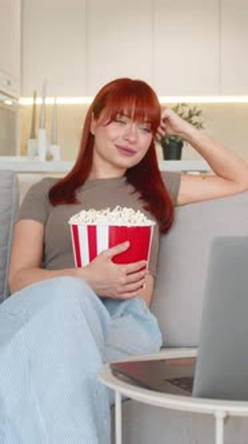 Une jeune femme avec du pop-corn regarde la bande-annonce du film sur un ordinateur portable rit à haute voix et profite d'un teaser amusant et de l'encourager