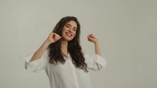 Mujer alegre con camisa blanca baila frente a la cámara Toma de estudio de una hermosa mujer de pelo largo