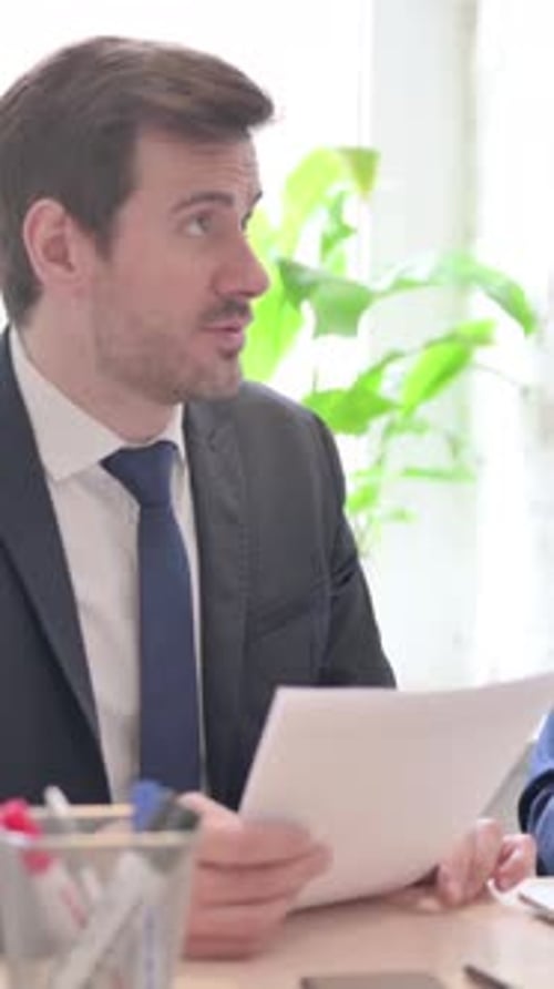 Man in Suit Talking with Colleague at Desk