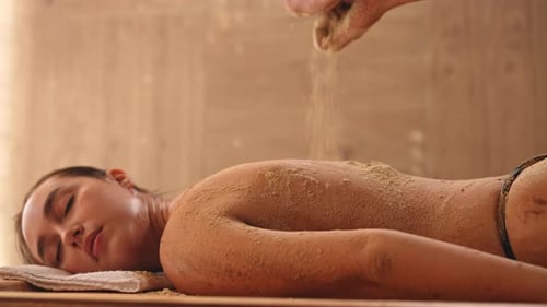 Tracking Shot of Spa Technologist Pouring Heated Sand on Back of Female Client to Scrubbing in