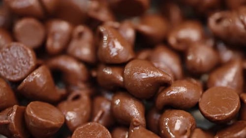 Stack of warm milk chocolate chips glistening in light macro close up 4k light sweeping and pan righ