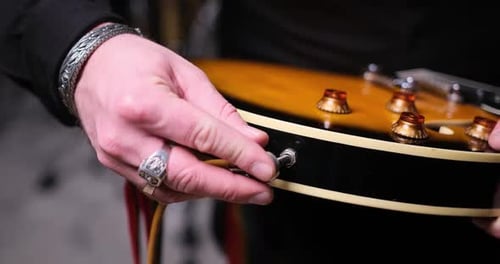 Gros plan de la main du guitariste branchant le câble audio dans une guitare électrique