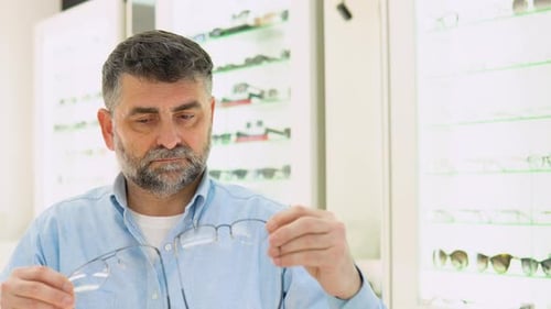 Hombre mayor de 50 a 60 años que elige anteojos mientras está sentado en una óptica