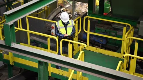 Overhead View of a Worker Inspecting Machinery in a Trash Sorting Facility