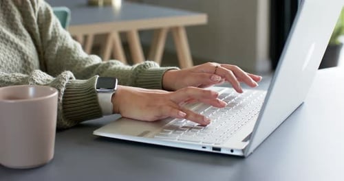 Typist settling at desk beside laptop is pressing keys while adjusting wrist during remote session
