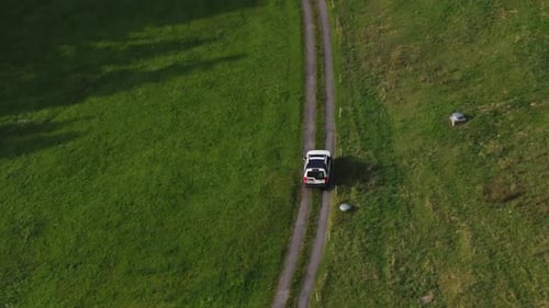 Aerial view of car driving on narrow countryside road through green meadow