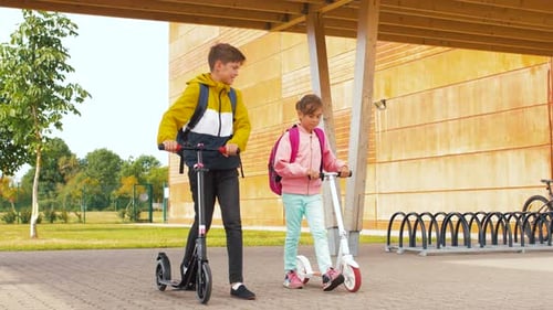 Happy elementary school kids with backpacks and scooters walking outdoors in spring