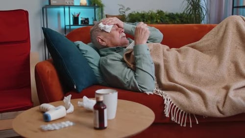 Un homme âgé malade souffrant de rhume ou d'allergies, allongé sur le canapé de la maison, éternue avec de la morve dans une serviette