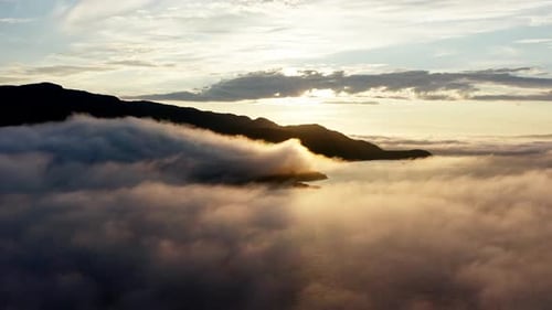 Drone Flying Above The Clouds Over The Sea With Rocky Mountain In Silhouette On A Golden Hour Sunris
