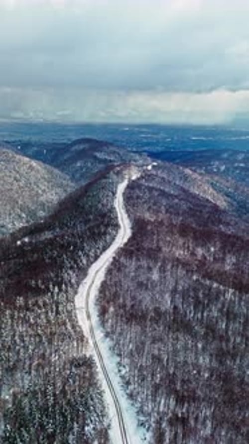Aerial View of Curved Road Through Winter Forest 4k