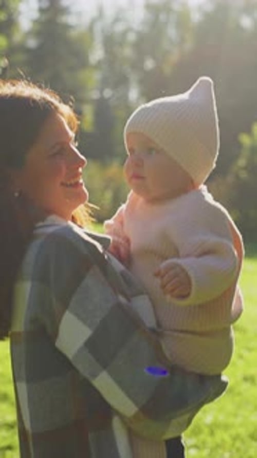 Mother Enjoys a Sunny Day in the Park Holding Her Baby Dressed in Warm Knitwear During Autumn