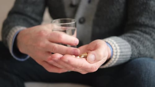 Hand Holding Pills With Glass of Water
