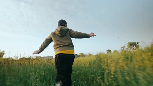 A Boy Child Running on the Grass in a Field at Sunset View From the Back