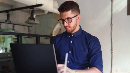 Jeune pigiste hipster attrayant travaillant à distance sur un ordinateur portable dans un loft café, un homme d'affaires naviguant