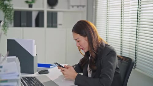 Asian happy businesswoman swiping on smartphone while working in office.