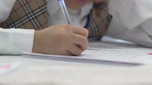 Child Writing on Paper in Classroom Close-Up