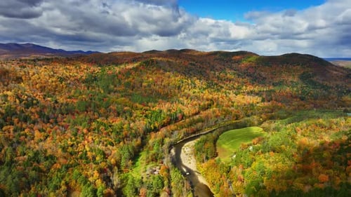 Bright thick autumn woods cover the mountainous landscape. Narrow river crosses the scenery