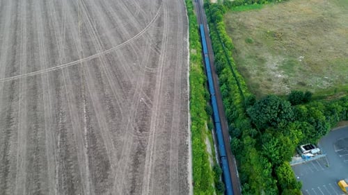 Drohnenaufnahme eines blauen Zuges auf einer von Bäumen gesäumten Eisenbahn, die durch die britische Landschaft fährt