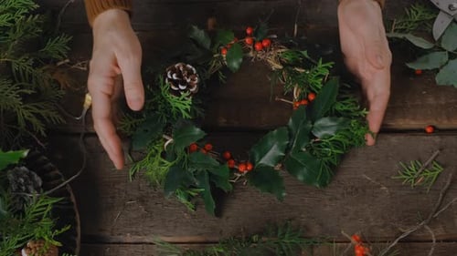 Arranging Natural Christmas Wreath on Wooden Table
