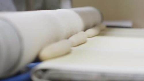 Fresh Bread Dough Moving On Conveyor Belt And Being Pressed By Roller. Low Angle, Close Up