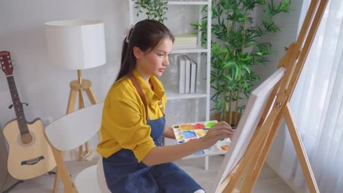 Asian young talented woman artist coloring on painting board in house.