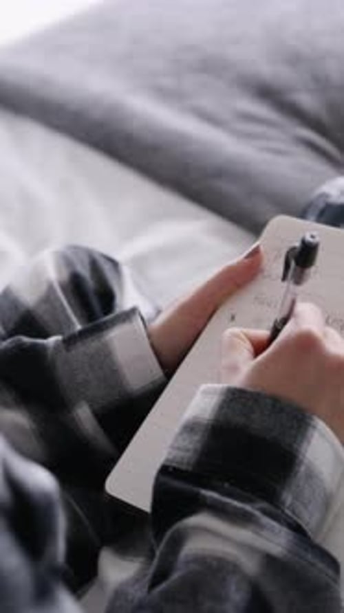 Woman, hands and writing with book in bed for diary, planning day or schedule in home