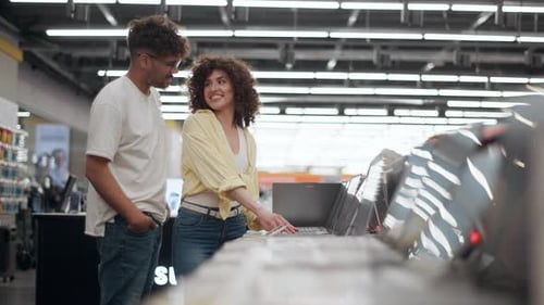Happy couple choosing laptop in electronics store in slow motion