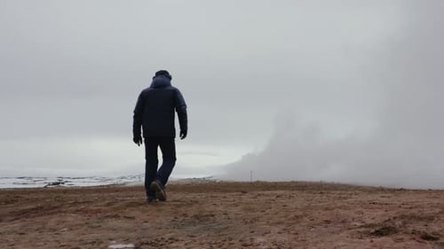 Tourist walk on orange volcanic gravel ground toward white smoke cloud