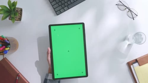 Top down view of man's hand using a mock up green screen tablet on a white desk