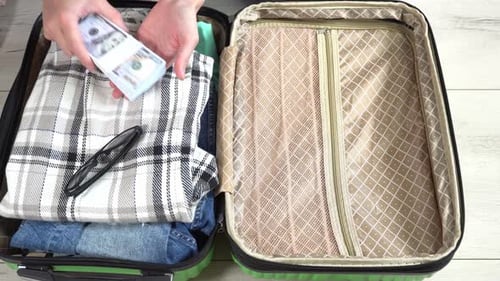 Man packing his suitcase for long journey with wad of money. Guy closes the green baggage case