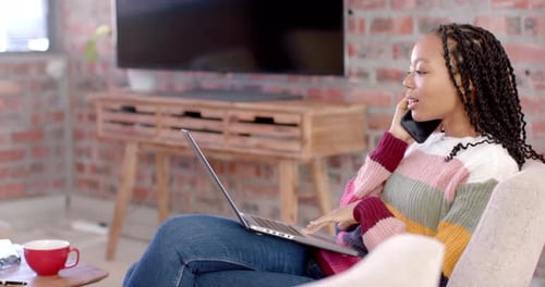 African american casual businesswoman using laptop and talking on smartphone in office