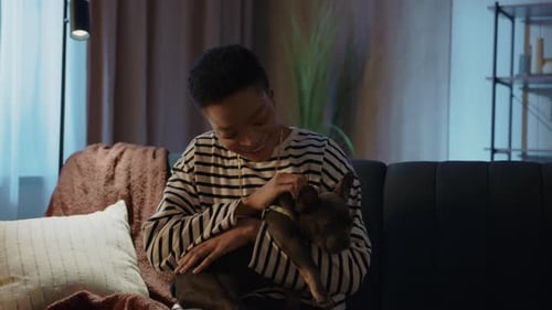 Happy African American Woman Hugs Dog with Love and Care Sitting on Couch at Home Relaxing