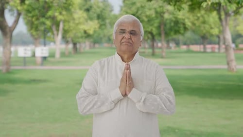 Religious Indian old man praying to God in park