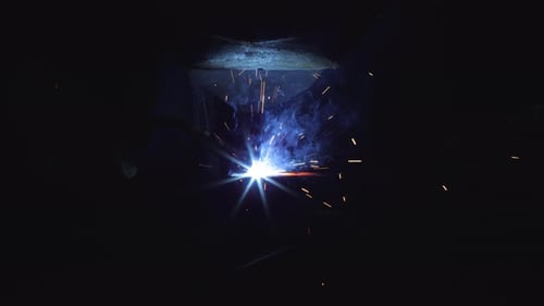 A blacksmith with a welding mask and welders leathers, is welding metal products in the garage, fire