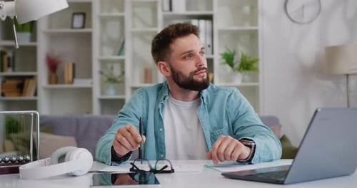 Bearded Man Contemplates Work at Desk With Laptop