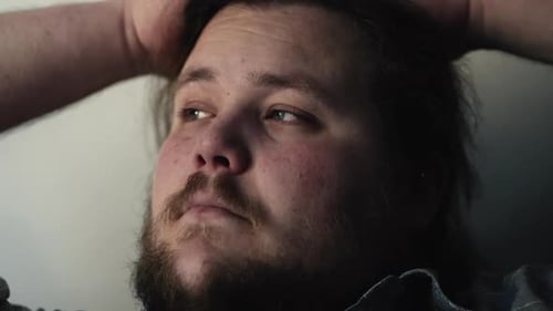 Un homme contemplatif en gros plan assis sur le canapé de la maison avec les mains derrière la tête