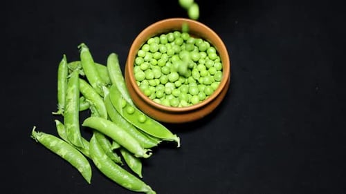 Fresh Green Peas peeled dropping in ceramic bowl with black background studio shot