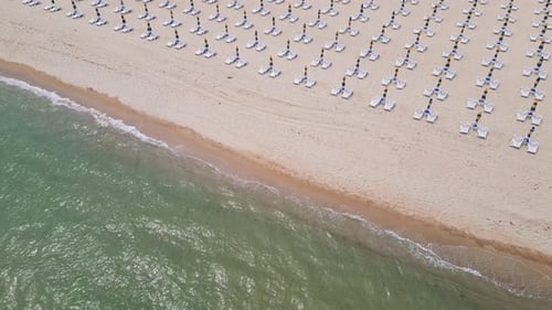 A Sandy Beach Stretches Along the Seaside Adorned with Empty Sun Loungers Aerial View