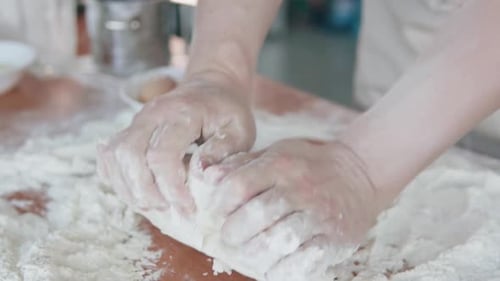 The cook in the bakery kneads the dough with his hands and begins to prepare bread.