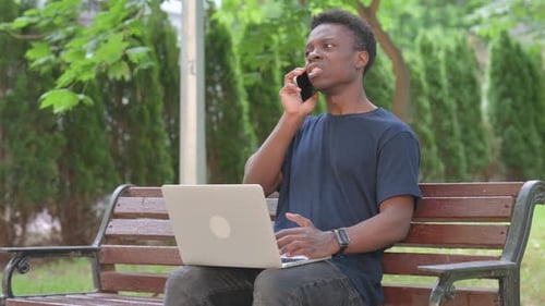 Angry African Man Talking on Phone While Using Laptop in Park