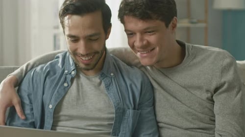 Two Young Men Relaxing on Couch Using Laptop