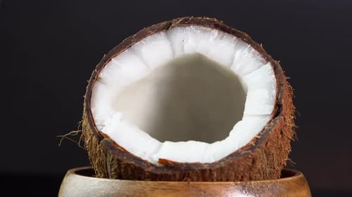Kokosnuss rotiert auf schwarzem Hintergrund in einer Holzschale. Gebrochene frische Kokosnuss mit spritzender Milch.