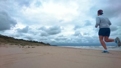 Der Mann läuft morgens am Strand. Windiger Morgen, welliges Meer, blaues Wasser, wolkig, fast stürmisch
.