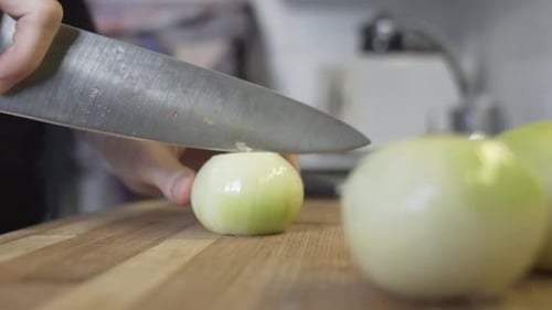 Slow-motion shot as taking an onion to the chopping board and cutting it in half, slicing it in the