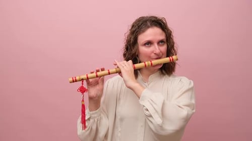 Frau hält Bambusflöte mit roter Quaste und spielt Musik. Studioporträt auf rosafarbenem Hintergrund. Tr