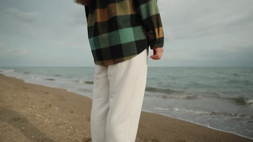 A lonely girl in cool weather on the sea stands by the water and looks into the distance. Slow-motio