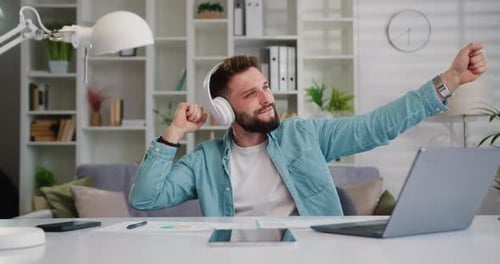 Man Dancing at Desk with Headphones and Laptop