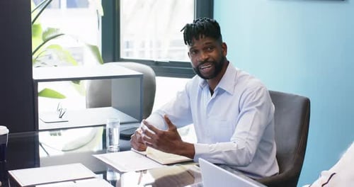 Smiling businessman sitting at desk in office meeting, holding pen and paper