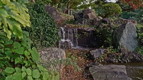 Kleiner malerischer Wasserfall über Felsen in einem traditionellen japanischen Garten