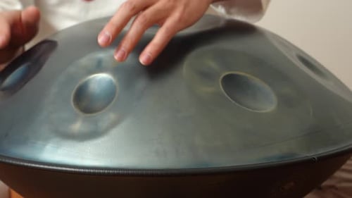 Close-up hand playing handpan (hang drum) in warm indoor studio